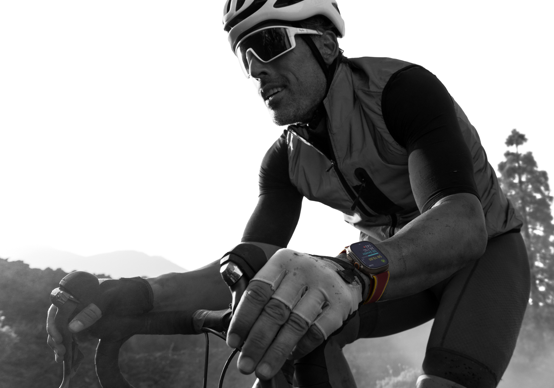 Uma pessoa anda de bicicleta na estrada usando um Apple Watch Ultra 4. A tela mostra métricas de ciclismo