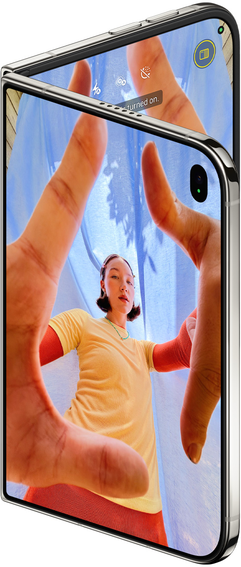 iPhone Duo branco-estrela parcialmente aberto mostrando o app Câmera na tela externa, com a câmera frontal Center Stage, e biblioteca do app Fotos na tela interna