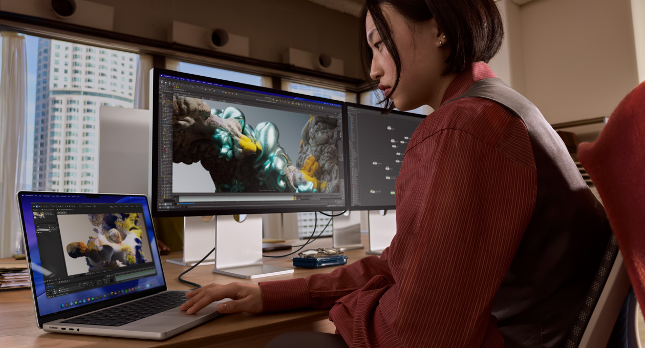 Člověk v kanceláři pracuje na MacBooku, ke kterému je přes port Thunderbolt 5 připojený Studio Display XDR