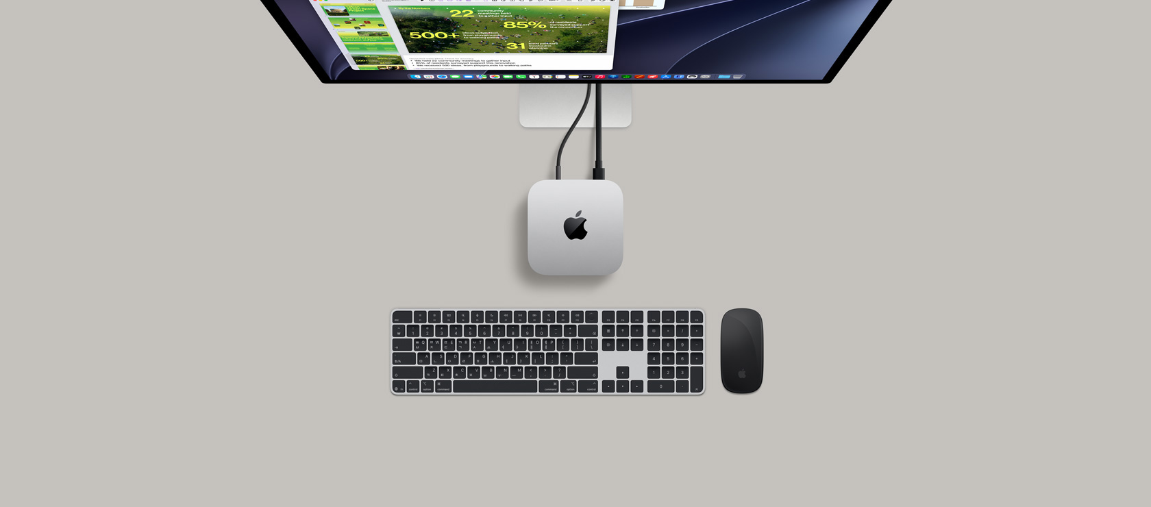 Mac mini를 위에서 바라본 모습. 실버 알루미늄 외장, 둥근 형태의 모서리, 중앙의 광택 나는 검은색 Apple 로고가 보이며, 코드가 연결되어 있습니다. 상단에 일부가 보이는 Studio Display가 보이며, 화면에는 캘린더 앱, 키노트 프레젠테이션과 막대그래프가 열려있고, Mac mini 아래에는 숫자 키패드 탑재형 Magic Keyboard, Magic Mouse가 보입니다.