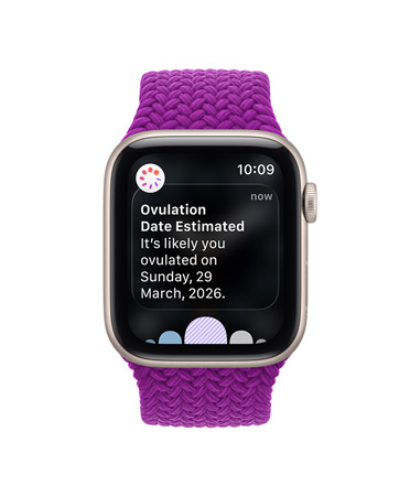 Apple Watch Series 12 z kopertą z aluminium w kolorze gwiezdnej szarości i plecioną opaską Solo w kolorze magenty, na ekranie powiadomienie o szacowanej dacie owulacji