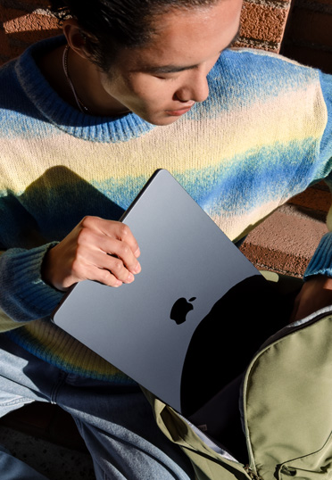 屋外で座っている学生。バックパックから閉じた状態のMacBookを取り出している