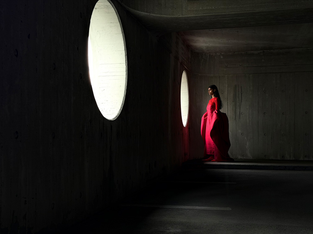 Una donna con un lungo vestito rosso fotografata in piedi in una stanza vuota. Nell’app Foto la lunghezza focale viene regolata a 48 mm, per mettere in evidenza le capacità del sistema di fotocamere Pro