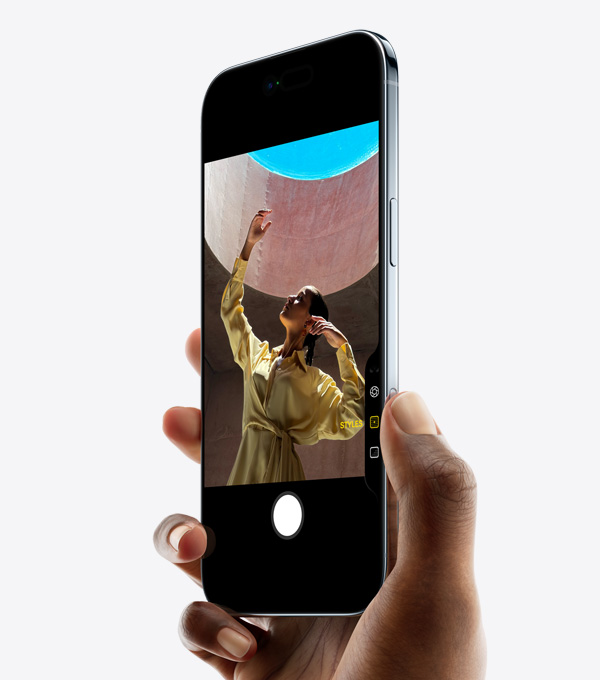 En hånd holder iPhone Air med tommelfingeren på knappen Kamerabetjening, vist forfra. Fra siden vises den meget tynde profil, Dynamic Island og sideknappen.